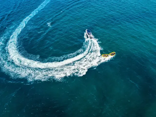 Vue du ciel, un bateau tracte une bouée dans un virage serré