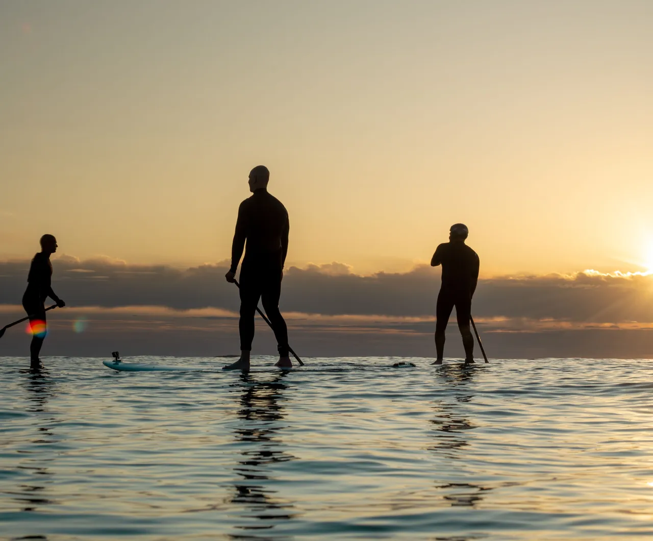 Trois paddles en silhouette sur l'eau, au lever du soleil